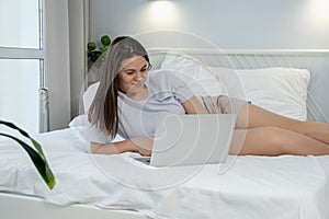 Young woman using laptop at home. Girl lying on bed in the morning