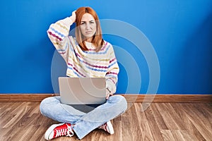 Young woman using laptop at home sitting on the floor confuse and wondering about question