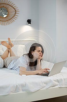 Young woman using laptop while lying on bed in bedroom at home