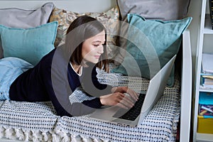 Young woman using laptop lying on sofa at home