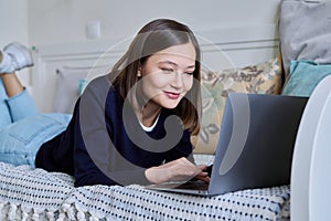 Young woman using laptop lying on sofa at home