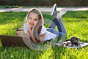 Young woman using laptop in the park lying on the green grass. Leisure time activity concept.