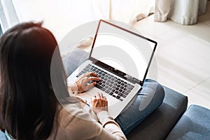 Young woman using laptop and relaxing on sofa in living room at cozy home in the morning