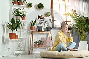 Young woman using laptop in room with home plants