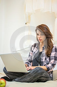 Young woman using laptop while sitting on bed.