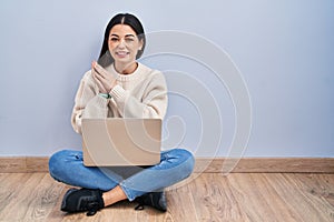 Young woman using laptop sitting on the floor at home clapping and applauding happy and joyful, smiling proud hands together