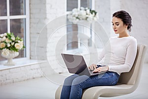Young woman using laptop while sitting on white chair
