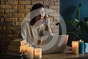 Young woman using laptop to work at home during electricity outage. Remote work at home concept. Woman speaking on the phone