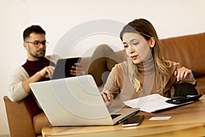 Young woman using laptop and young man using digital tablet while sitting on sofa at home