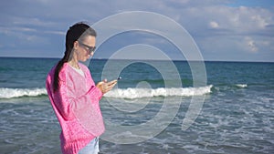 Young woman using mobile phone on the beach. Girl taking selfie by smartphone on the seashore