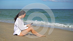 Young woman using mobile phone on the beach. Girl taking selfie by smartphone on the seashore