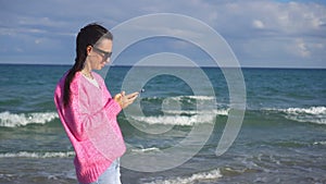 Young woman using mobile phone on the beach. Girl taking selfie by smartphone on the seashore