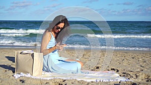 Young woman using mobile phone on the beach. Girl taking selfie by smartphone on the seashore