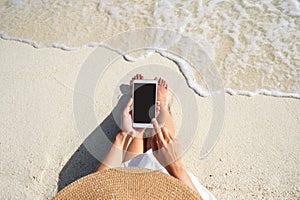 Young woman using mobile phone at beautiful tropical white sand beach with wave foam and transparent sea, Summer vacation and