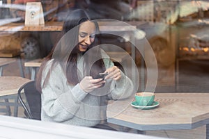 Young woman using mobile phone in cafe throuth glass window