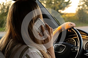 Young woman using mobile phone while driving car on highway road during sunset. Womandriver has accident calling with