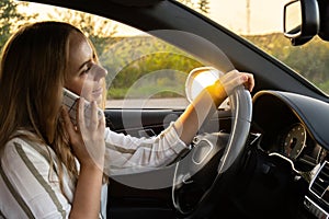 Young woman using mobile phone while driving car on highway road during sunset. Womandriver has accident calling with