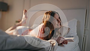 Young woman using mobile phone at home. Smiling happy female lying in bed typing