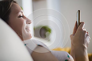 Young woman using mobile phone at home smiling lying in sofa