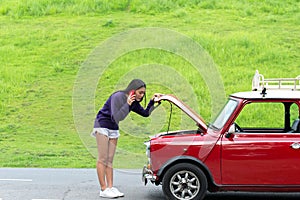 Young woman using mobile phone while looking at broken down car