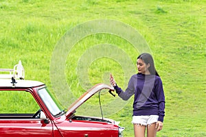 Young woman using mobile phone while looking at broken down car