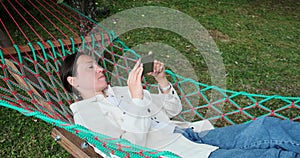 Young woman using mobile phone while lying on hammock