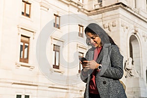 Young woman using mobile phone in the street. Latin girl wear a smart watch and text on the phone