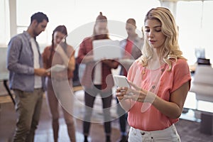 Young woman using mobile phone with team working in background