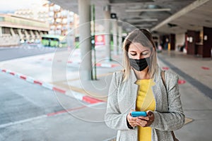 Young woman using mobile phone while waiting at bus station during coronavirus outbreak - Focus on face