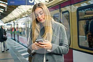 Young woman using mobile phone while waiting for train at railway station