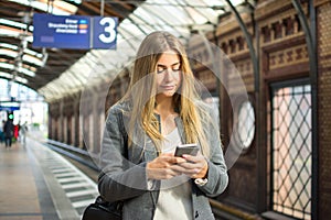 Young woman using mobile phone while waiting for train at railway station