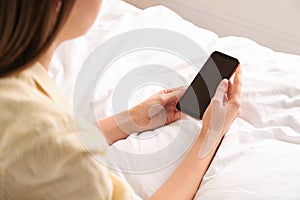 Young woman using modern smartphone on bed at home
