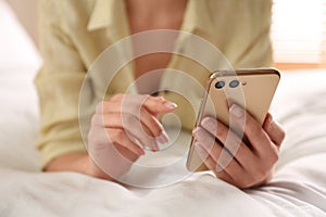 Young woman using modern smartphone on bed at home