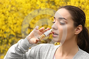 Young woman using nasal drops near blooming tree. Allergy concept