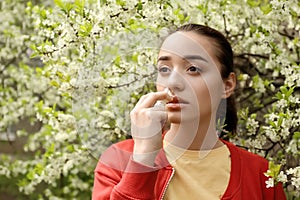 Young woman using nasal drops near blooming tree. Allergy concept