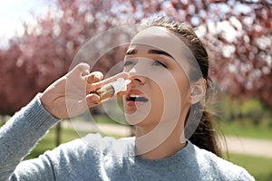 Young woman using nasal drops near blooming trees. Allergy concept