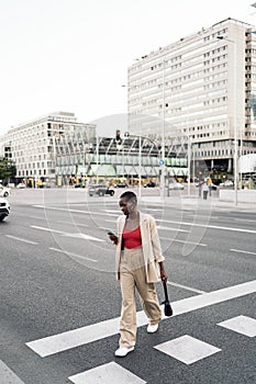 Young woman using phone while crossing the street