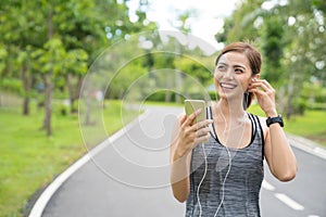 Young woman using phone for listening to music. Fitness runner girl listening to music with earphones on phone wearing smartwatch.