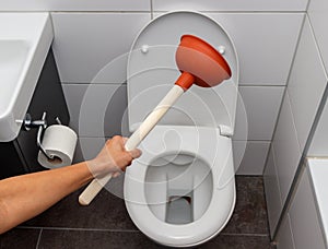 Young woman using plunger to unclog a toilet bowl