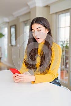 Young woman using red smartphone sending a message scared in shock with a surprise face, afraid and excited with fear expression