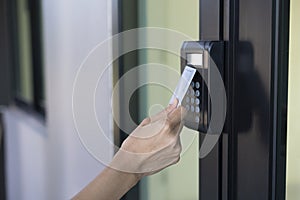 Young woman using RFID tag key, fingerprint and access control to open the door in a office building