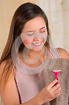 Young woman using a shaver on a brown jogging suit, in bath background