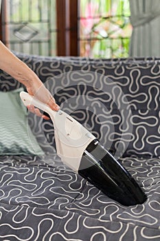 Young woman using a small manual vacuum cleaner while cleaning textile upholstery on the couch
