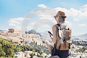 Young woman using smart phone in Athens with Acropolis at the background. Traveler girl enjoying vacation in Greece.