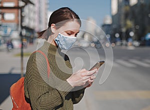 Young woman using smart phone in the city wearing face mask for air pollution, flu, virus, influenza, coronavirus