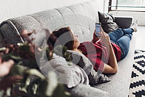 Young woman using smart phone while lying on the couch at home