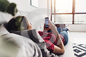 Young woman using smart phone while lying on the couch at home