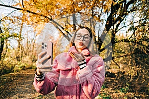 Young woman using smartphone in autumn park , heaving video call, communicate with friends or family