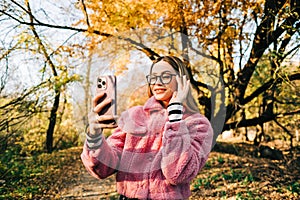 Young woman using smartphone in autumn park , heaving video call, communicate with friends or family