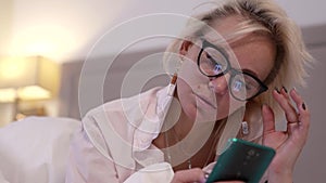 young woman is using smartphone in bed at evening, shopping online and surfing internet, portrait